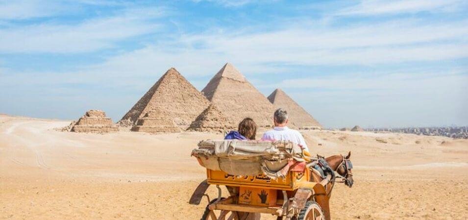 Couple on a historic ride in a cart past the Great Pyramids of Giza, ideal for planning a trip to Egypt