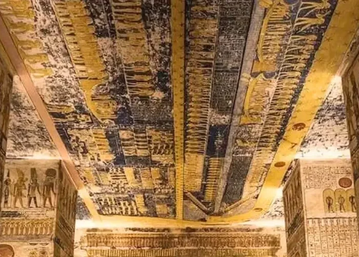 Interior view of the Tomb of Ramesses V and VI in The Valley of the Kings, Egypt, featuring ornate hieroglyphics on stone pillars and a vibrant blue astronomical ceiling depicting the Book of Day and Night.