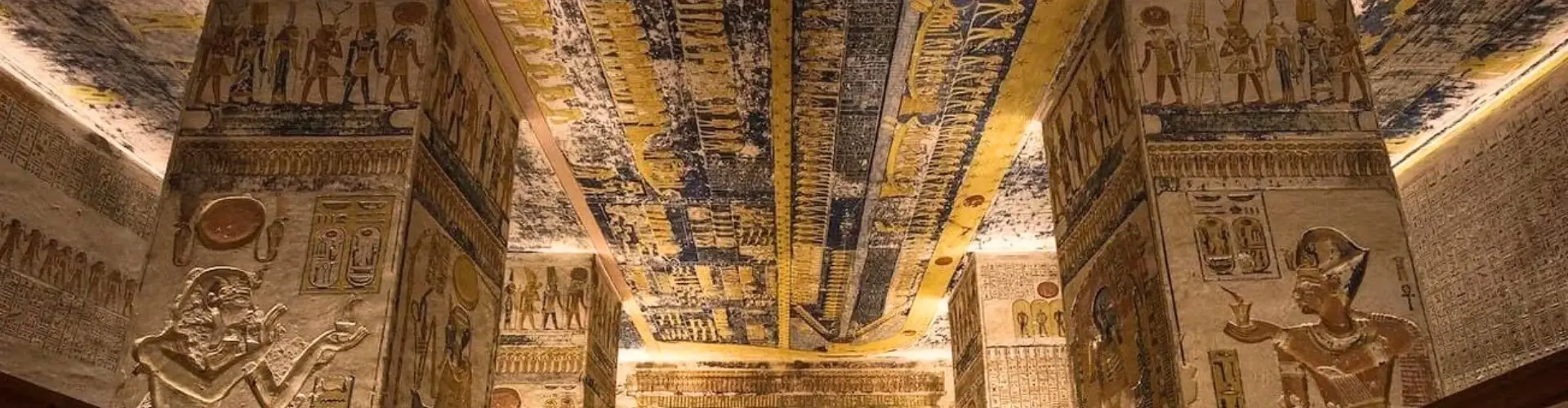 Interior view of the Tomb of Ramesses V and VI in The Valley of the Kings, Egypt, featuring ornate hieroglyphics on stone pillars and a vibrant blue astronomical ceiling depicting the Book of Day and Night.