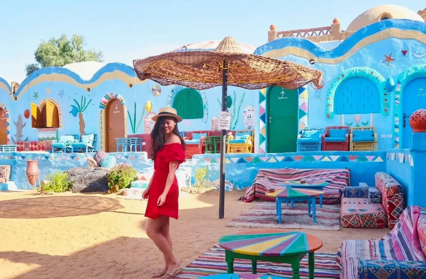 Nubian Village Aswan: A Complete Guide to Gharb Soheil's Colorful Culture 3 A female tourist wearing a red dress standing in a colorful sandy courtyard in the Nubian Village in Aswan, Egypt.