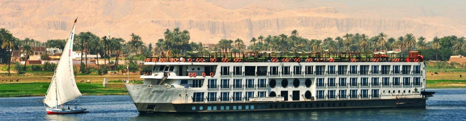 A traditional felucca and a modern ship on the river, a highlight of a Nile Cruise Itinerary.