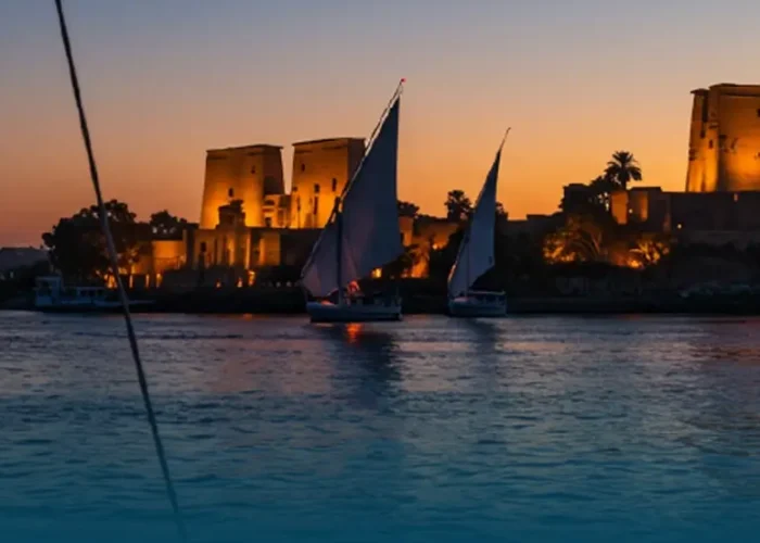 Sunset view of an illuminated Egyptian temple during a Nile cruise from Luxor to Aswan with feluccas.