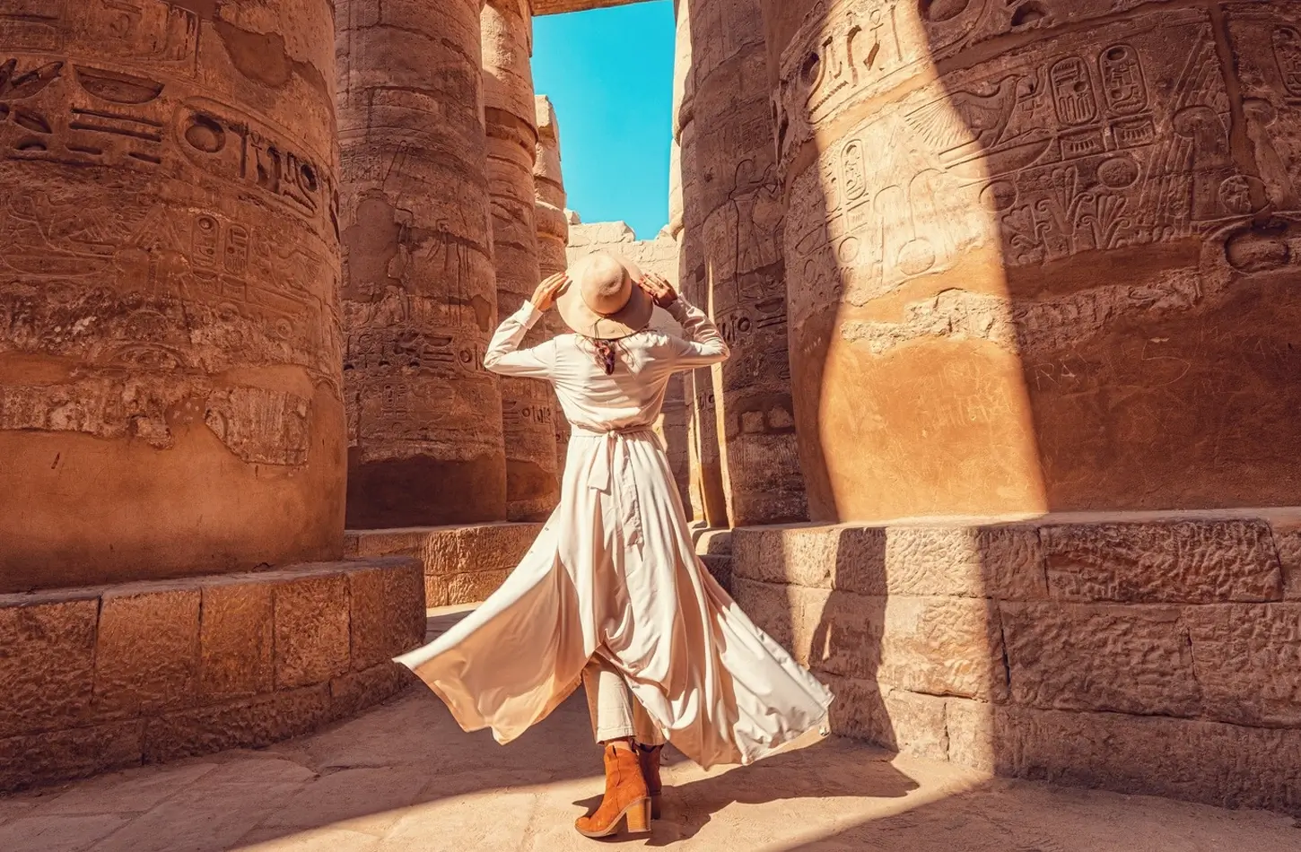 Woman in a sun hat exploring the towering columns and hieroglyphics inside the ancient Luxor Temple