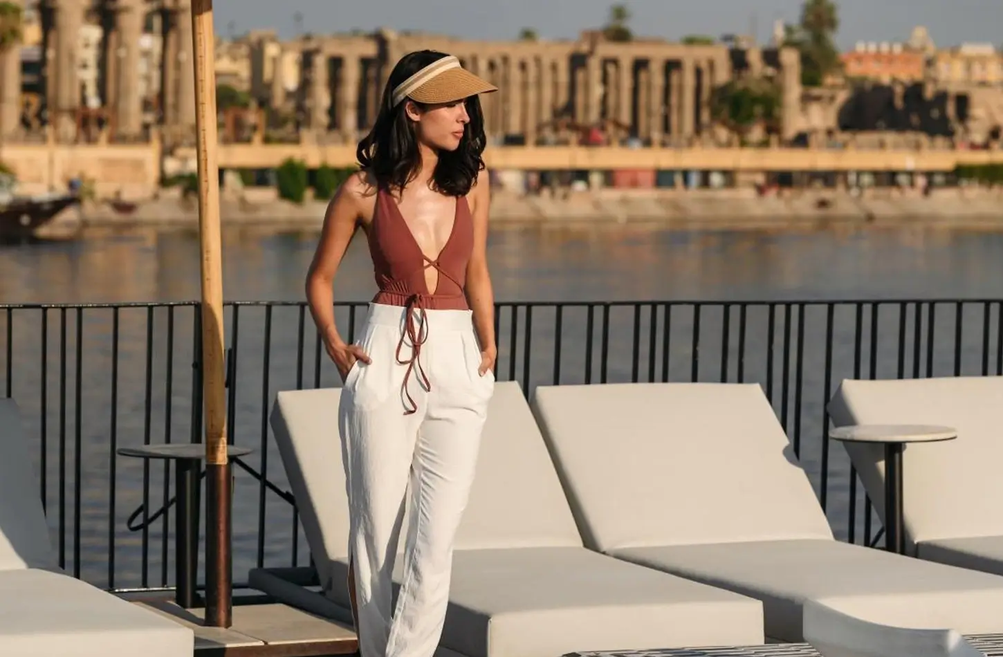 "Woman on a luxury Nile cruise ship deck overlooking ancient Egyptian temples in Luxor during a river tour."