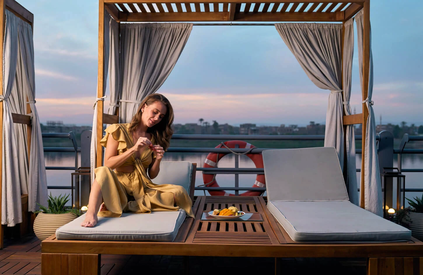 Tourist in a yellow dress relaxing on a Nile cruise ship deck at sunset in Egypt.