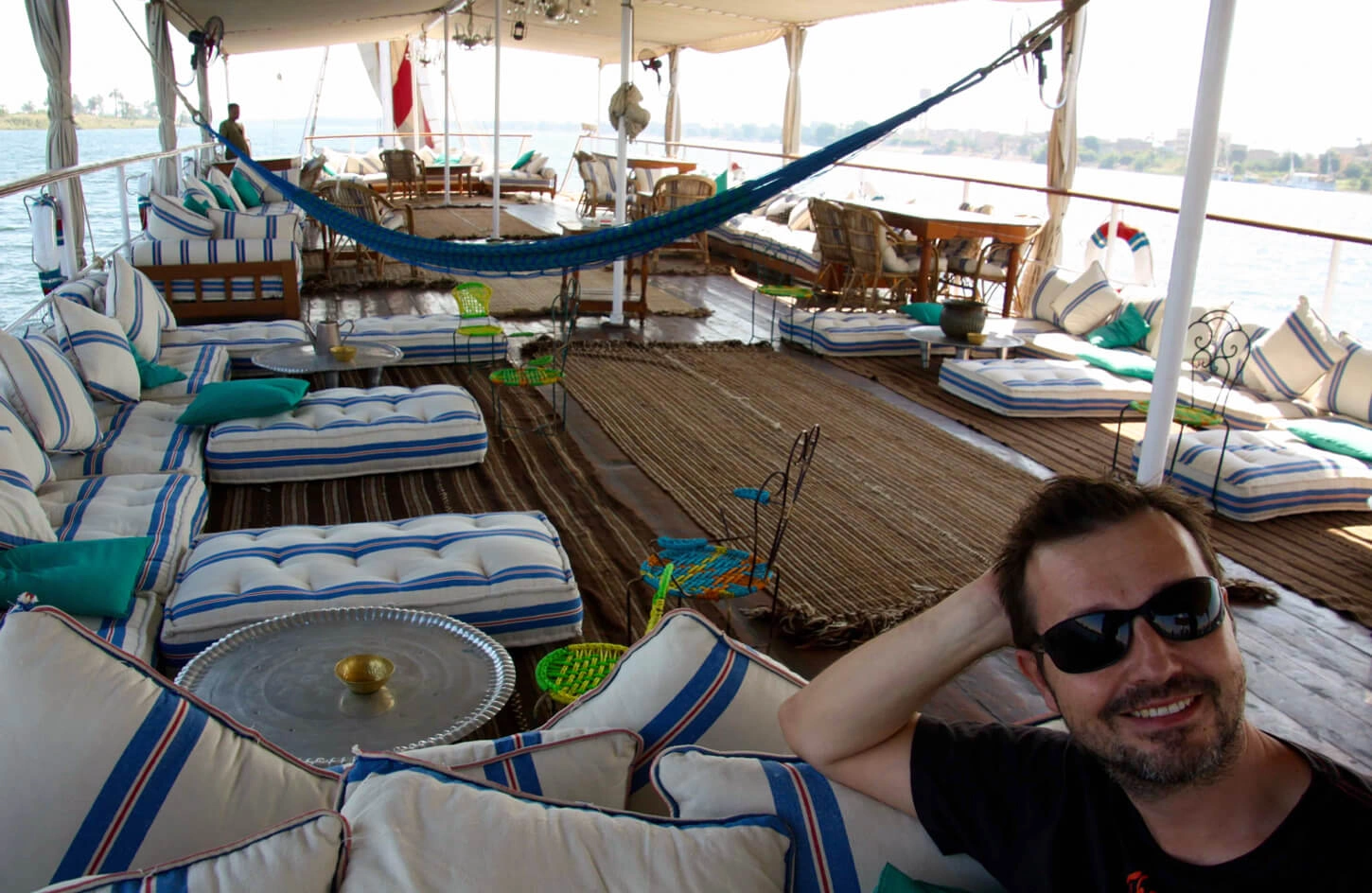 A traveler in a yellow dress sits on a wooden cabana bed on a boat deck at dusk.