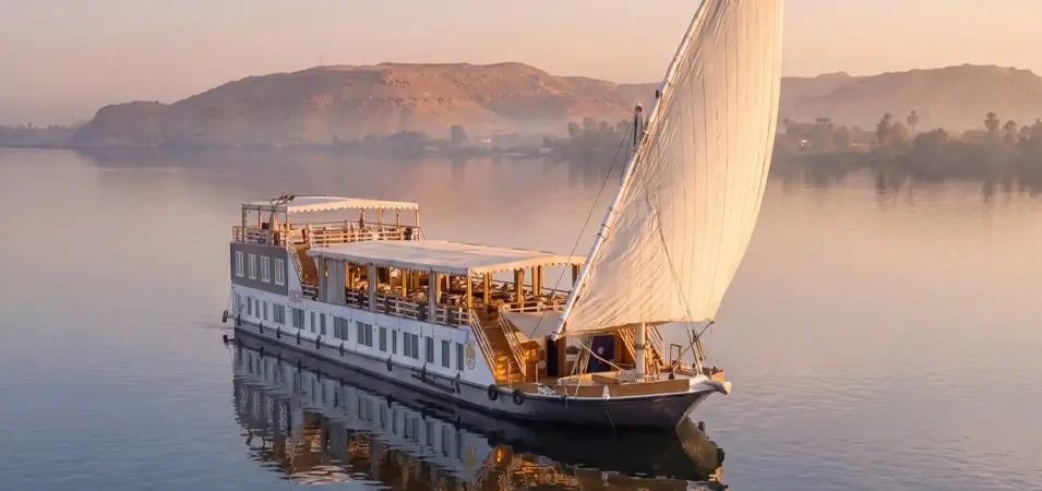 A traditional Dahabiya sailboat sailing peacefully on the Nile River at sunrise